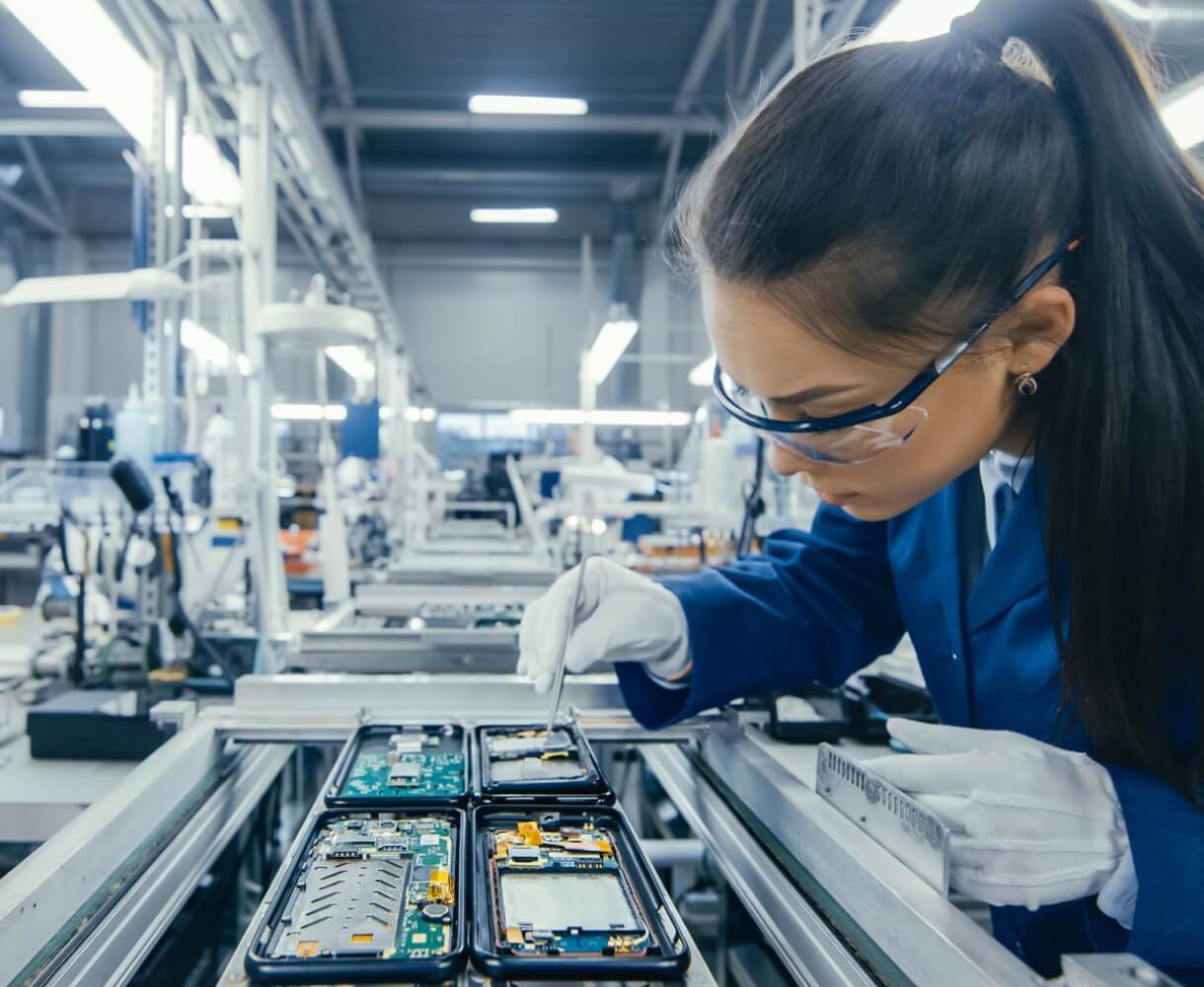 A female technician in a blue uniform meticulously assembles components in an industrial manufacturing setting.