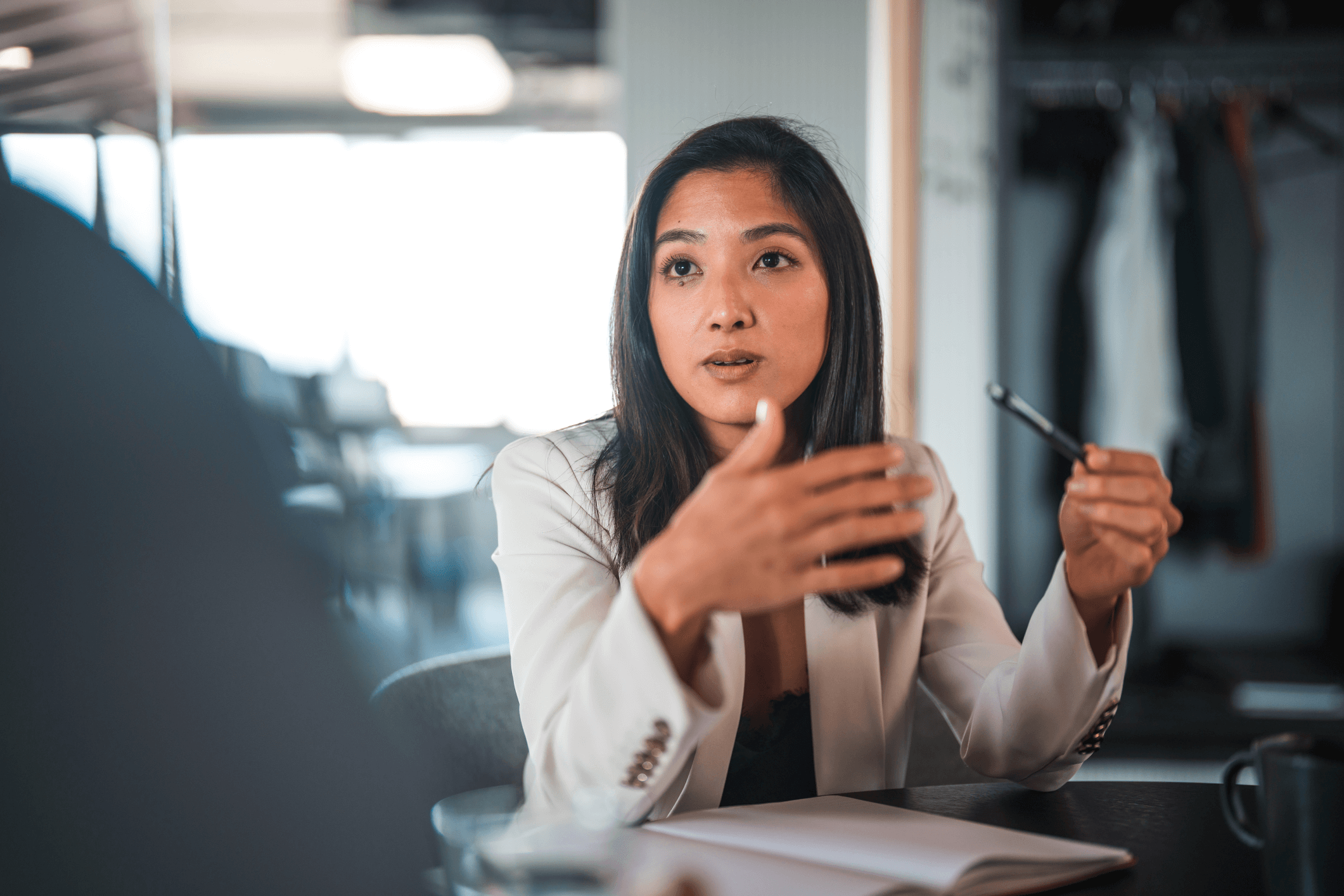A confident Asian businesswoman actively explaining a point during a meeting in a well-lit office.