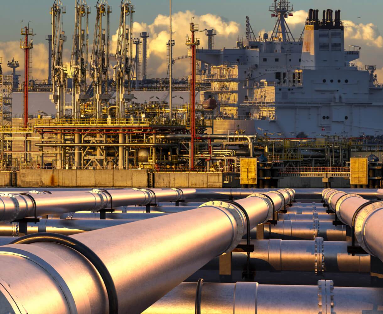 A panoramic view of an industrial complex with pipelines and refinery structures at sunset.
