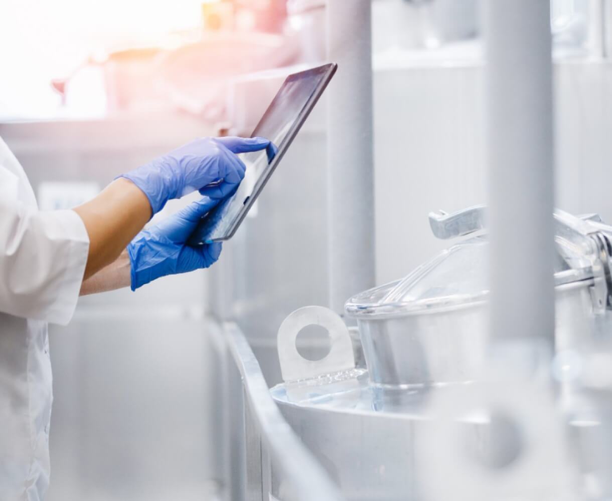 A lab technician in protective gear uses a tablet to monitor processes in a industrial manufacturing environment.