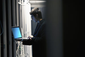 Male IT programmer with laptop in server room