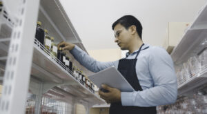 Handsome business owner or staff using computer tablet checking product inventory on shelf stock in grocery store