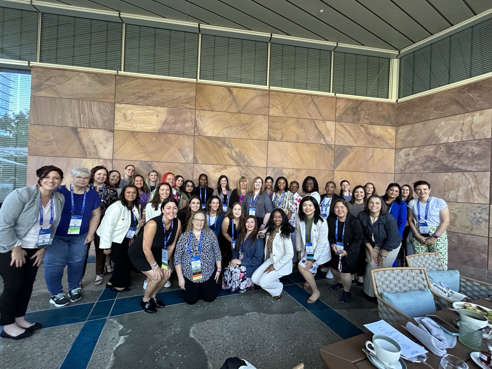 A group of women in fincrime smiling and posing for a photo in front of a wall during the Women’s Breakfast event hosted by SymphonyAI at the ACAMS Assembly 2024.