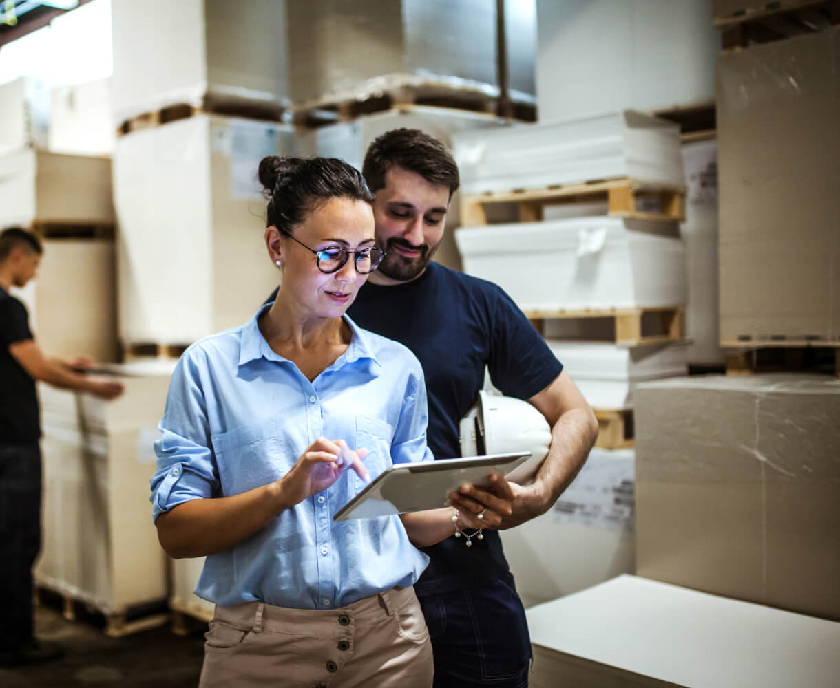 Woman and man look over tablet in a warehouse environment.