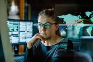 A female data analyst focused on screens displaying complex data visualizations and world maps.