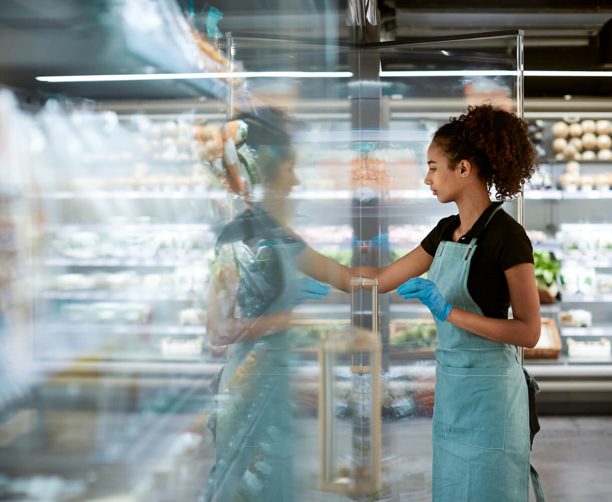 Young woman arranging products in a grocery store cooler.