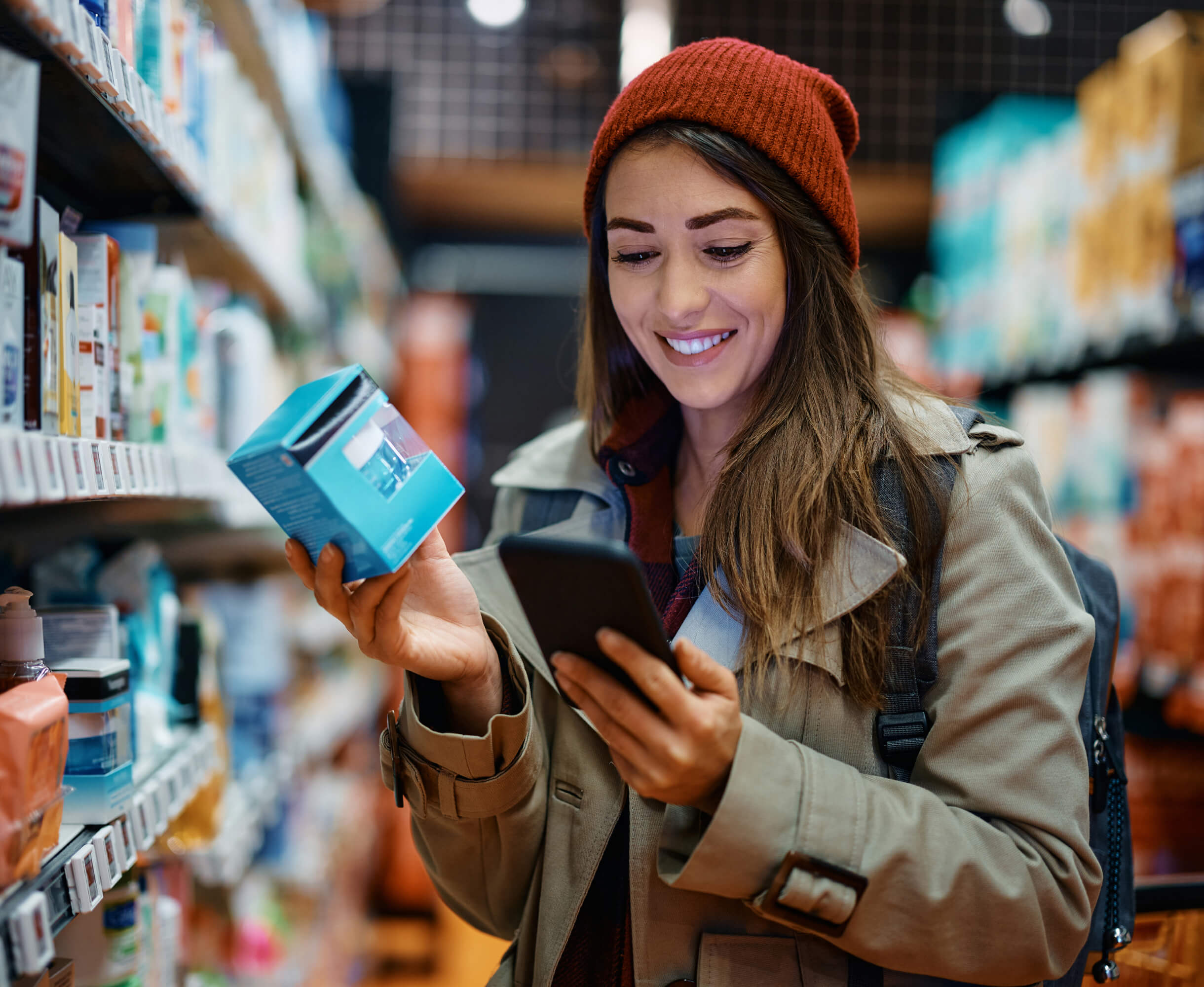 A woman in a grocery store aisle compares product information on her smartphone.