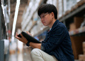 Young man with glasses taking inventory in a warehouse.