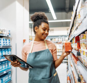 Young black woman smiles while restocking grocery shelf.